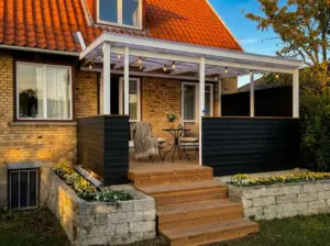Overdækket træterrasse med hyggelig belysning og sorte læhegn, perfekt til sommeraftener